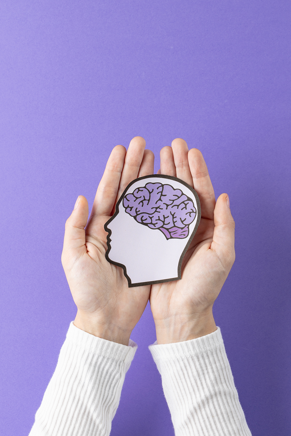 Hands holding head silhouette with brain on purple background with copy space. Medicine, healthcare and science concept.